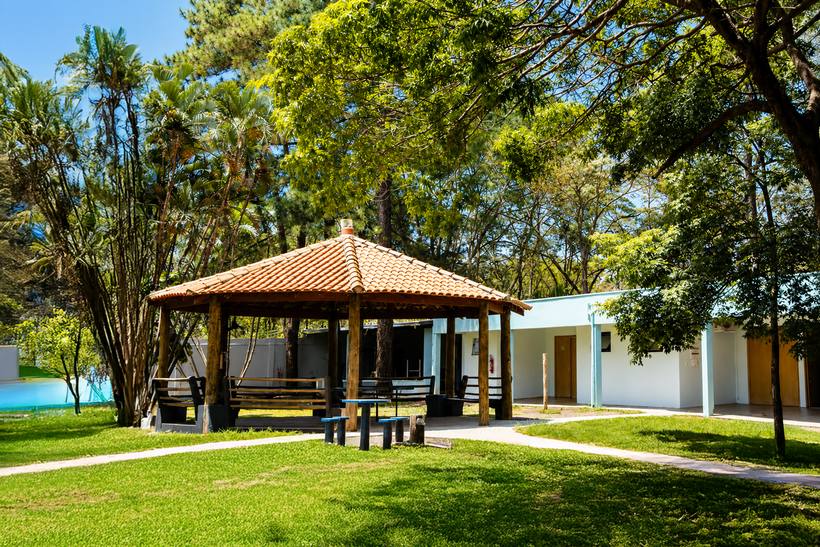 Quiosque coberto com mesas para refeições e convívio ao ar livre, entre árvores.